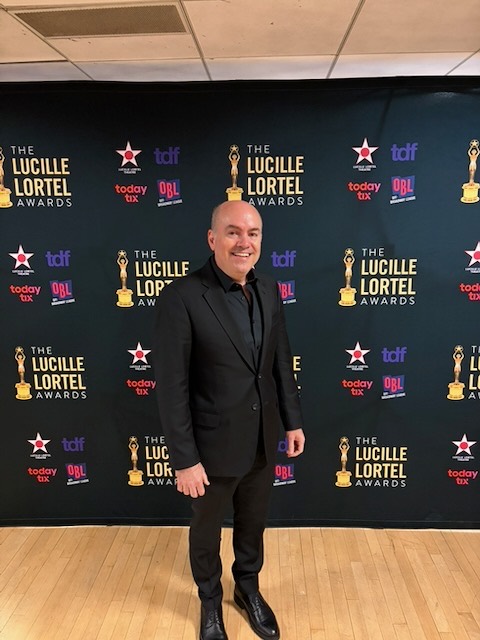 Brian Guy at the Lucille Lortel Awards in front of the awards step-and-repeat